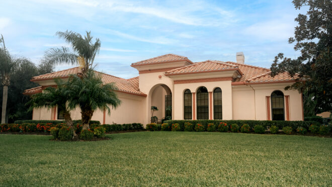 Exterior house painting in Sarasota: peach stucco Mediterranean-style home with a terracotta tile roof, palm trees and a green lawn under a blue sky