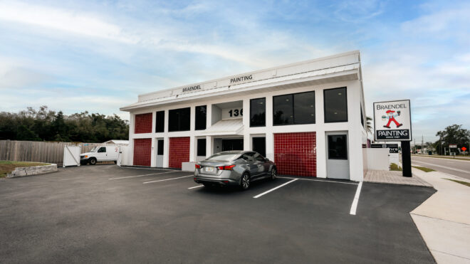 Two-story Braendel Painting office building finished in white exterior paint with red tile accents and a company sign under a blue sky