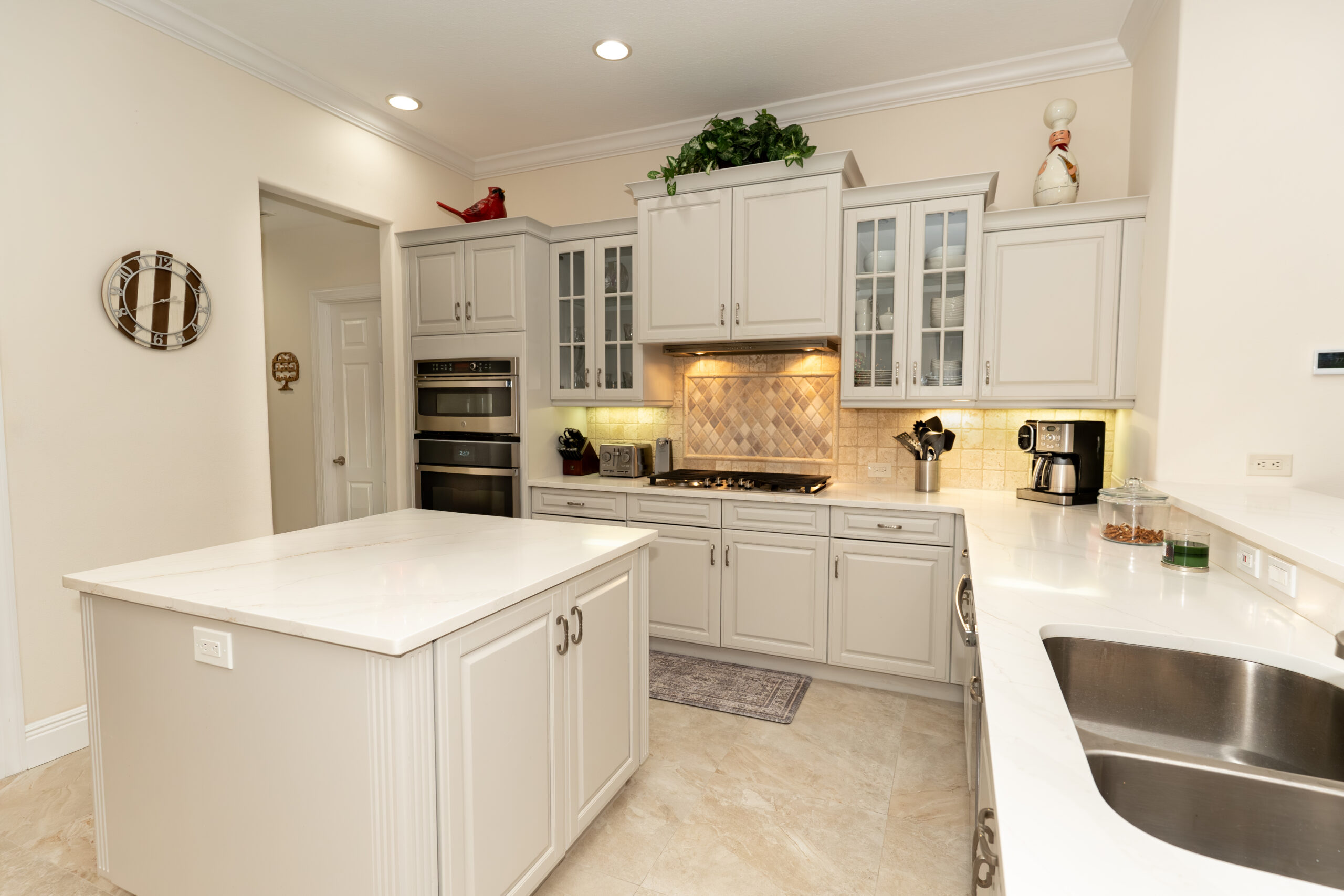 Interior house painting in Sarasota: kitchen with freshly painted walls, white cabinets, a center island, stone backsplash and tile flooring
